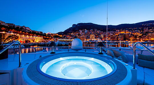 Night view from a luxury yacht deck with illuminated hot tub and Monaco city lights in the background, representing Monaco residence and Monaco residency lifestyle.