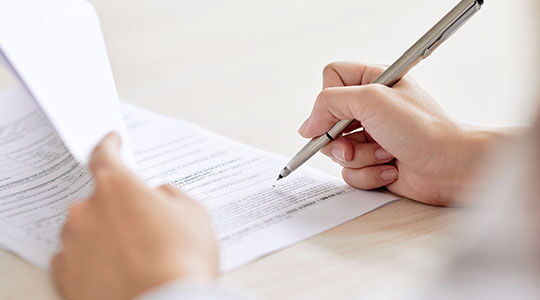 Close-up of hands signing official paperwork, representing how to apply for residency and complete a residency permit application.