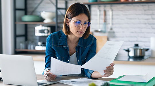 Woman reviewing paperwork at a desk with a laptop, representing residency permit document checks when applying for residency in Monaco.